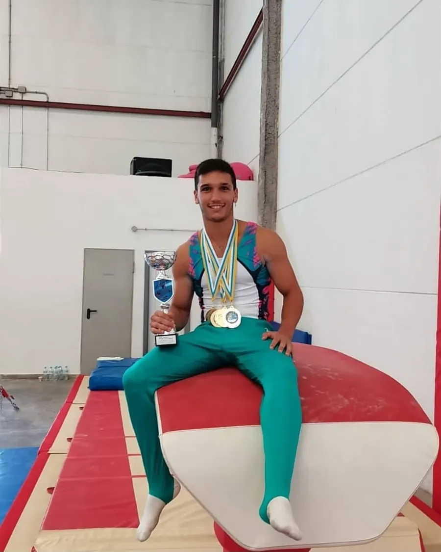 Alejandro sentado en el potro con medallas y un trofeo